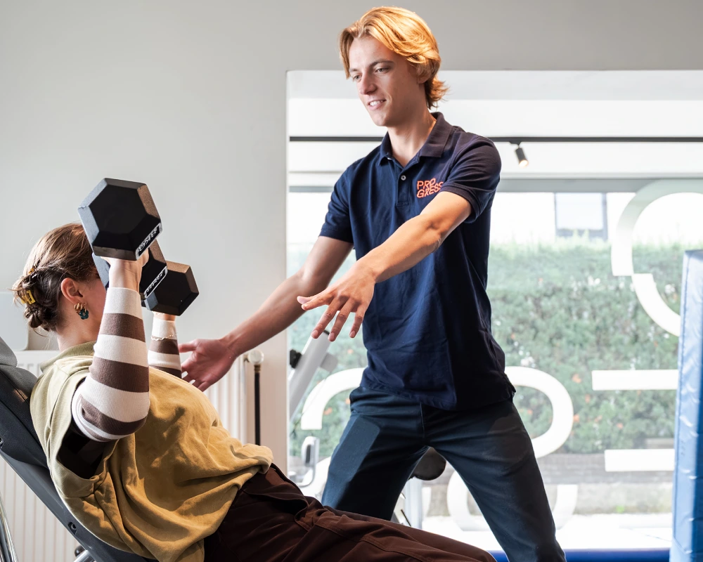 Een kinesist en patiƫnt tijdens een oefensessie in de oefenzaal van kinepraktijk Progress Brugge.